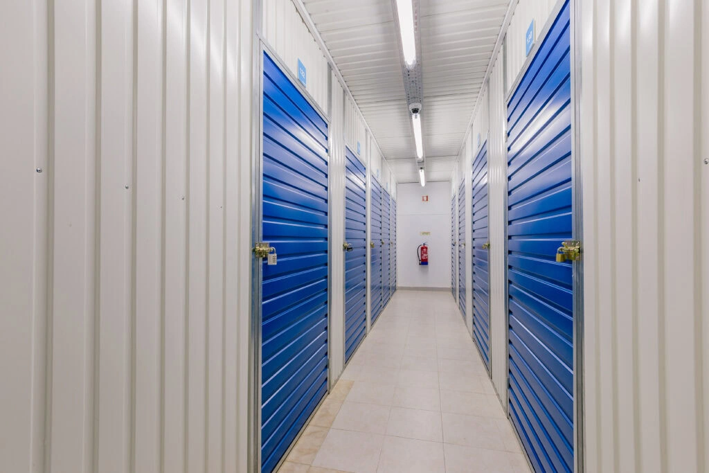 Allstorage Self storage Um corredor na instalação Allstorage ostenta portas roll-up azuis em ambos os lados. O corredor bem iluminado, com luzes fluorescentes e um extintor de incêndio montado de forma proeminente na parede branca no final, leva a opções adicionais de autoarmazenamento. O piso de ladrilho bege claro adiciona um acabamento limpo. Arrecadacoes e armazens para alugar - Allstorage selfstorage Allstorage Self storage Um corredor na instalação Allstorage ostenta portas roll-up azuis em ambos os lados. O corredor bem iluminado, com luzes fluorescentes e um extintor de incêndio montado de forma proeminente na parede branca no final, leva a opções adicionais de autoarmazenamento. O piso de ladrilho bege claro adiciona um acabamento limpo. Arrecadacoes e armazens para alugar